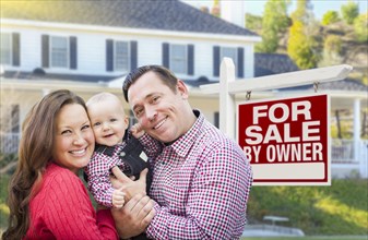 Happy young family in front of for sale by owner real estate sign and house