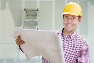 Smiling contractor holding blueprints inside home construction site