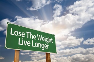 Lose the weight live longer green road sign with dramatic clouds