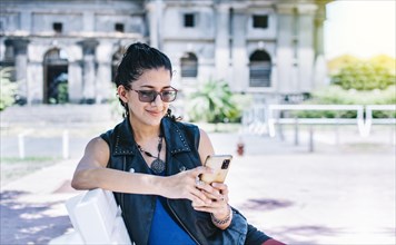Urban style girl sitting on a bench with her cell phone