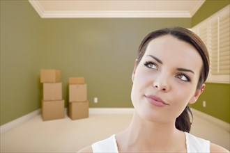 Attractive daydreaming young woman in empty green room with boxes