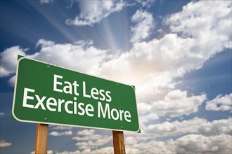 Eat less exercise more green road sign with dramatic clouds