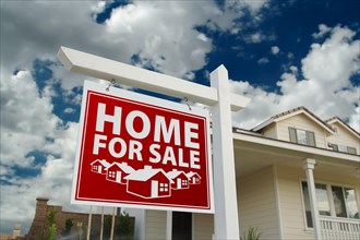 Red home for sale real estate sign and house against a blue sky