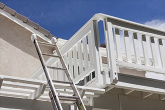 Construction ladder leaning on white house deck with blue sky behind