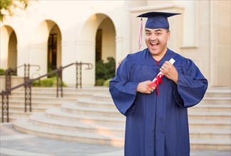 Hispanic male with deploma wearing graduation cap and gown on campus