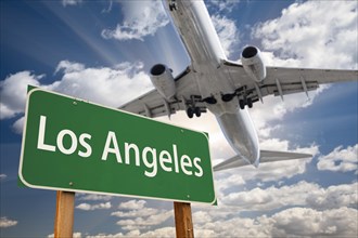 Los angeles green road sign and airplane above with dramatic blue sky and clouds