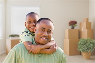 Happy african american father and son in room with packed moving boxes