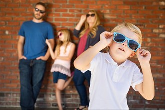 Cute young caucasian boy wearing sunglasses with family behind