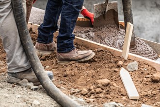 Construction workers pouring and leveling wet cement into wood framing