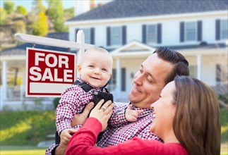 Happy young family in front of for sale real estate sign and house