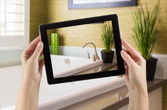 Female hands holding computer tablet in bathroom with photo on screen