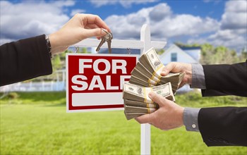 Man handing woman thousands of dollars for keys in front of house and for sale real estate sign