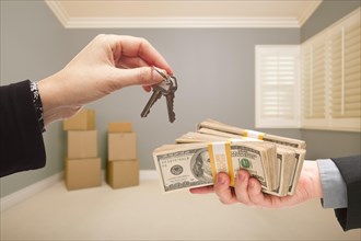 Man and woman handing over cash for house keys inside empty gray room with boxes