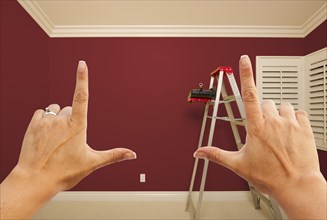 Hands framing deep red painted room wall interior with ladder