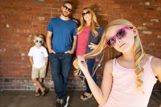 Cute young caucasian girl wearing sunglasses with family behind