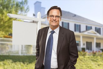 Male real estate agent in front of blank home for sale sign and house