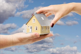 Female hand reaching for a house on a partly cloudy sky background
