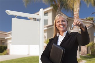Female real estate agent handing over the house keys in front of a beautiful new home and blank real estate sign