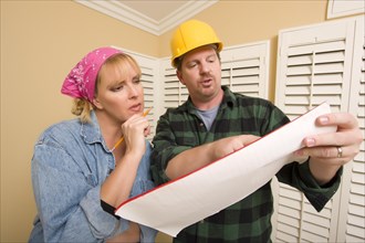Male contractor in hard hat discussing plans with woman in room