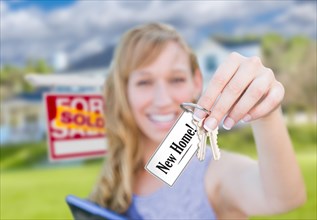 Woman holding new house keys with new home card in front of sold real estate sign and home