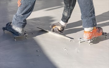 Worker wearing spiked shoes smoothing wet pool plaster with trowel