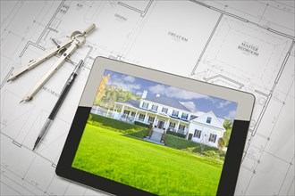 Computer tablet showing finished house sitting on house plans with pencil and compass