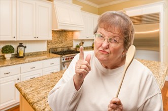 Senior adult woman scolding with the wooden spoon inside kitchen