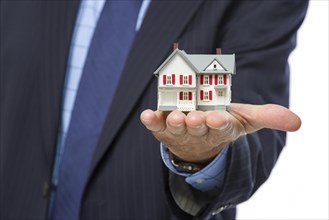 Close up of male real estate agent holding out A miniature house in his hand