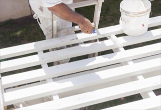 Painter rolling white paint onto the top of A home patio cover