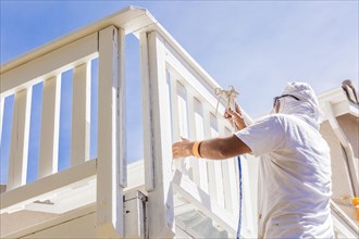 House painter wearing facial protection spray painting A deck of A home