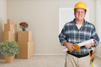 Contractor with plans and hard hat inside empty room with moving boxes
