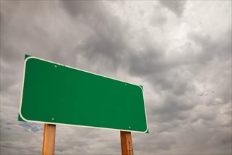 Blank green road sign over dramatic stormy clouds