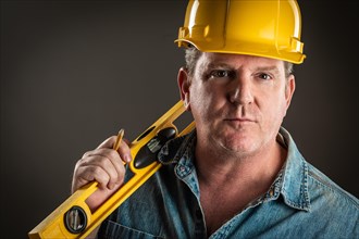 Serious contractor in hard hat holding level and pencil with dramatic lighting