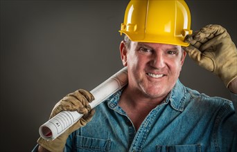 Smiling contractor in hard hat holding floor plans with dramatic lighting