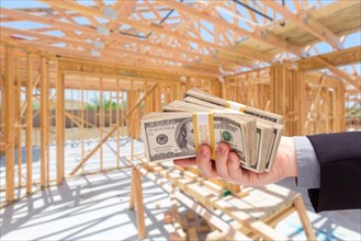 Hand with stacks of cash on site inside new home construction framing