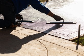 Construction worker smoothing wet cement with trowel tools