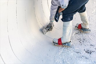 Worker wearing spiked shoes smoothing wet pool plaster with trowel