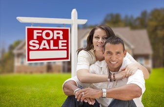 Young happy hispanic young couple in front of their new home and for sale real estate sign