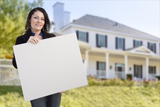 Smiling hispanic female holding blank sign in front of beautiful house