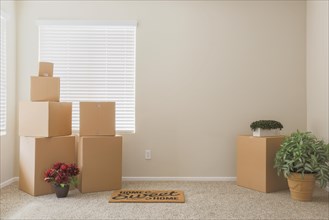 Variety of packed moving boxes and potted plants and welcome mat in empty room with room for text
