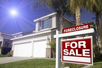 Red foreclosure for sale real estate sign in front of house with blue star-burst in sky