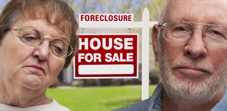 Depressed senior couple in front of foreclosure real estate sign and house