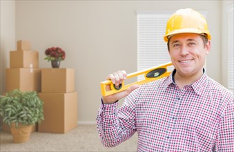 Happy male construction worker in room with moving boxes holding level