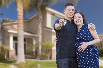 Happy hispanic couple in front of new home showing off their house keys