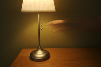Abstract of modern lamp against green wall on wood table. ghosted hand reaches for light switch