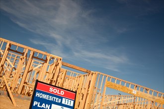 Sold lot real estate sign at new home framing construction site against deep blue sky