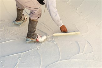 Worker wearing spiked shoes smoothing wet pool plaster with trowel