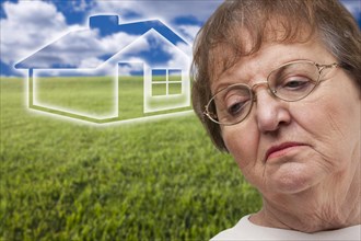 Melancholy senior woman with green grass field and ghosted house behind her