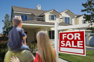 Young family looking at a beautiful new home with a for sale real estate sign in front