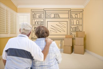 Hugging senior couple in empty room with shelf design drawing on wall